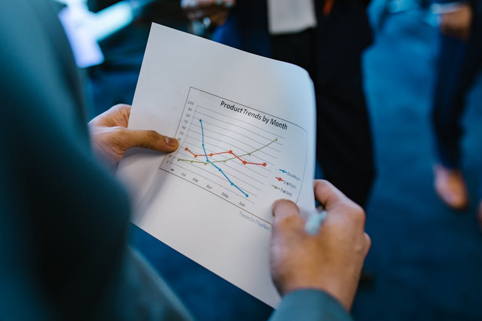 Close-up of hands holding a paper with a line graph showing product trends by month during a business meeting.
